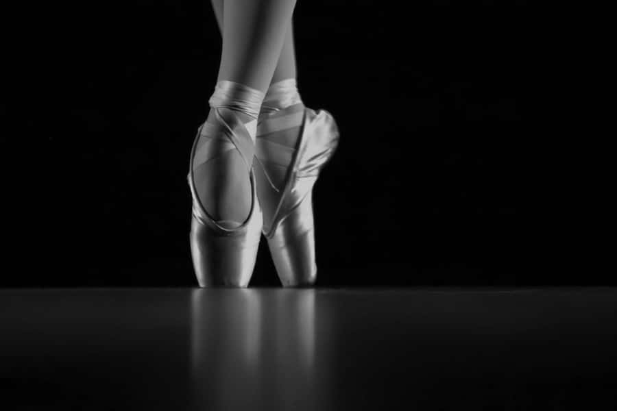 The Elegance Of Ballet: Gleaming Pointe Shoes In The Darkness Wallpaper