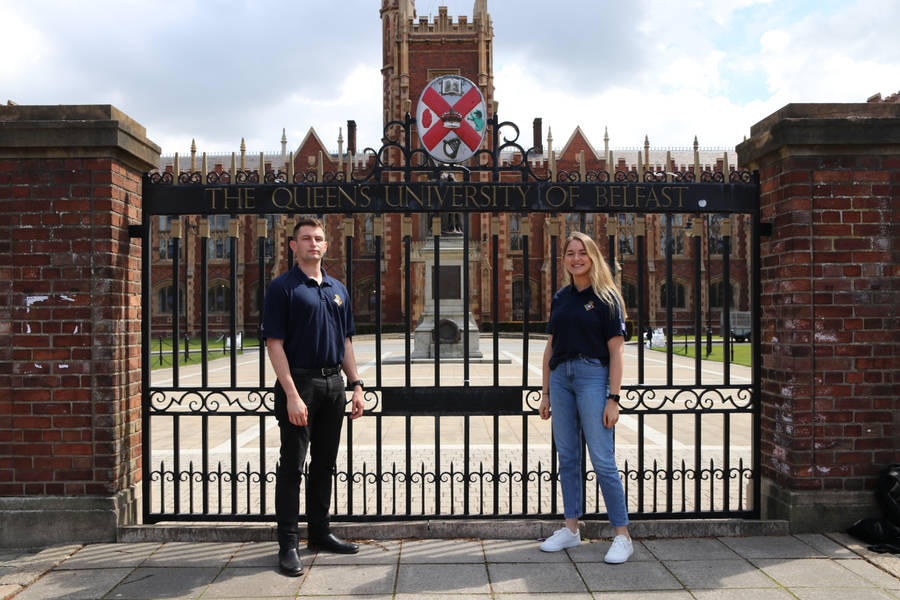 Two People Standing In Front Of A Gated Entrance Wallpaper