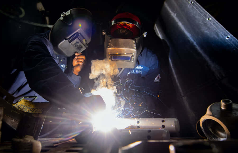 Two Welders Working On A Metal Piece Wallpaper