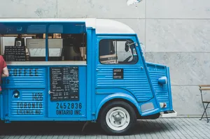 A Blue Food Truck With A Man Standing Next To It Wallpaper