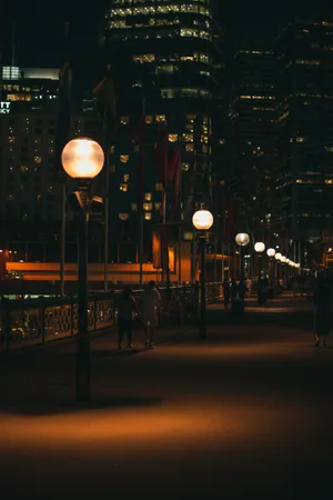 A City At Night With People Walking Along The Sidewalk Wallpaper