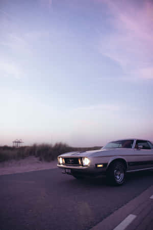 A Classic Car Driving Down The Road Wallpaper