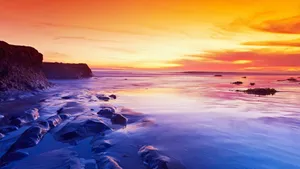 A Colorful Sunset Over The Ocean And Rocks Wallpaper