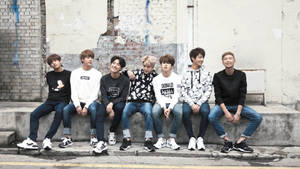 A Group Of Young Men Sitting On The Sidewalk Wallpaper