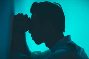 A Man Is Leaning Against A Wall With His Hand On His Face Wallpaper