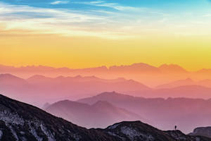 A Person Standing On Top Of A Mountain At Sunset Wallpaper