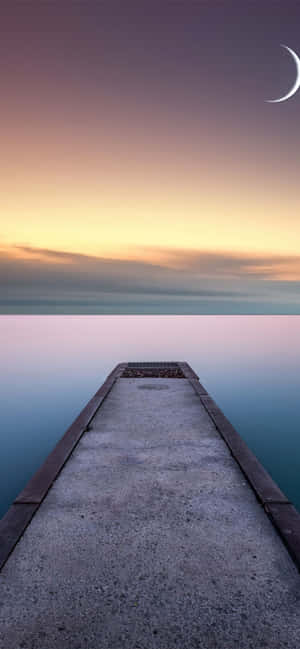 A Pier Leading To The Water With A Crescent Moon Wallpaper