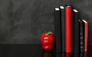 A Spacious Library With Blackboard, Apples, Books And Chairs Wallpaper