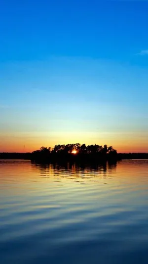 A Sunset Over A Lake With Trees On It Wallpaper