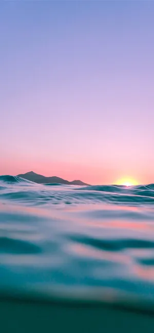 A Sunset Over The Ocean With Waves And Mountains Wallpaper