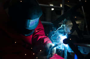 A Welder Is Welding Metal In A Dark Room Wallpaper