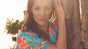 A Woman In A Floral Dress Leaning Against A Wooden Pole Wallpaper