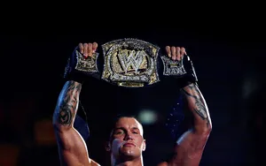 A Wrestler Holding Up A Wwe Championship Belt Wallpaper