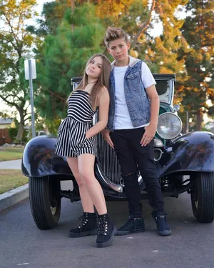 A Young Girl And Boy Standing Next To An Old Car Wallpaper