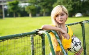 A Young Woman Leaning Against A Fence With A Soccer Ball Wallpaper