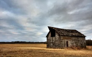An Old Barn Sits In A Field Under A Cloudy Sky Wallpaper