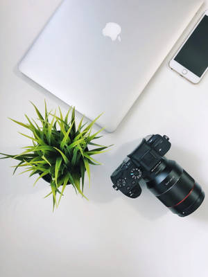 Caption: Apple Devices And Camera On A Wooden Desk Wallpaper