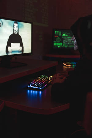 Enigmatic Cybersecurity: Man In Hacker Mask On Television Wallpaper