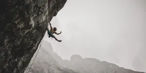 Fearless Adventurer Conquers The Cliff Amidst Stormy Skies Wallpaper