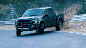 Ford F-150 Raptor - A Black Truck Driving On A Track Wallpaper