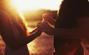 Holding Hands While Facing Each Other At Sunset Wallpaper