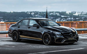 Luxurious Elegance - Shiny Black Amg Against Orange Fence Wallpaper