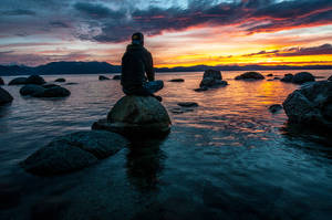 Man Sitting Alone On Rocky Beach Wallpaper