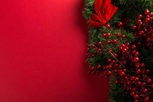 Perfect For The Holiday Season: A Red Christmas Wreath Set Against A White Wall Wallpaper