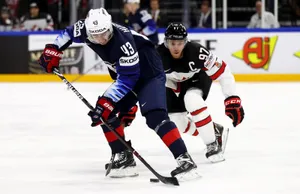 Quinn Hughes Dribbling Hockey Puck In Front Of Player From Team Canada Wallpaper
