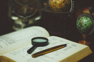 Reference Book With Magnifying Glass And Pen Wallpaper