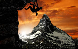 Silhouetted Man Rock Climbing Under Orange Sky Wallpaper