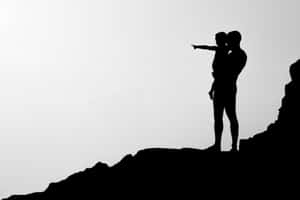 Silhouetteof Coupleon Mountain Pointing Wallpaper