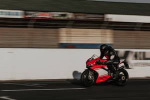 Speed Thrill: Bike Rider Racing Through A Track Wallpaper