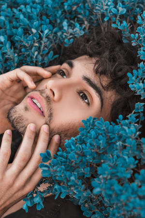 Stylish Man In Dynamic Blue Pose Amidst Foliage Wallpaper