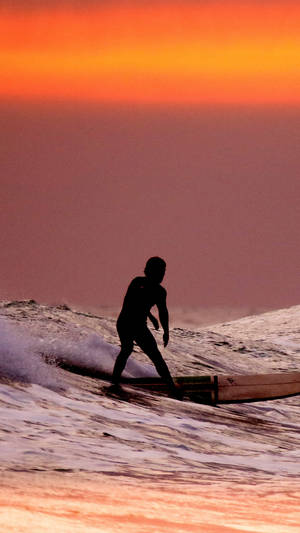Surfing Under An Orange Sunset Sky Wallpaper