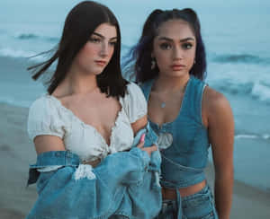 Two Women Standing On The Beach Wearing Denim Wallpaper